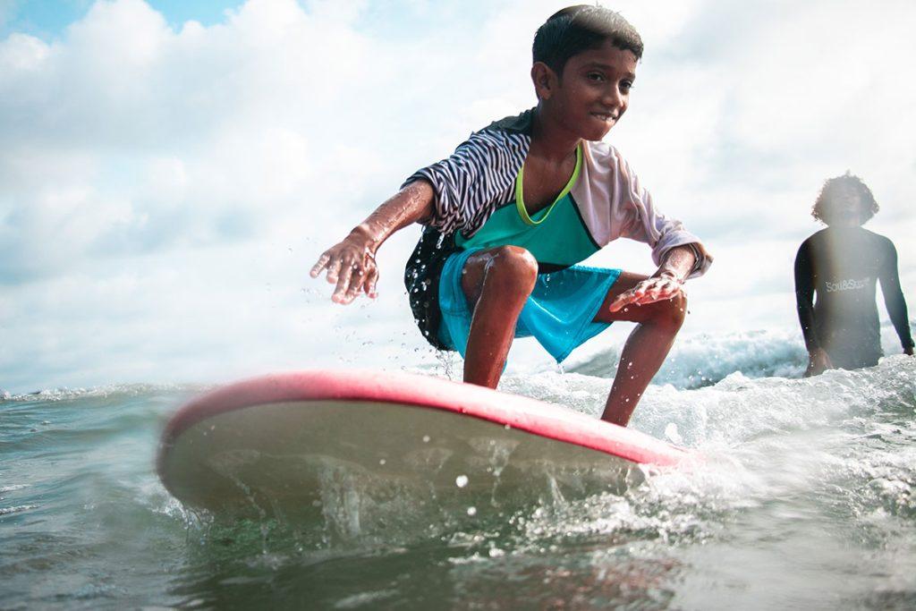 Child riding a gentle wave in Kerala with surf coach support